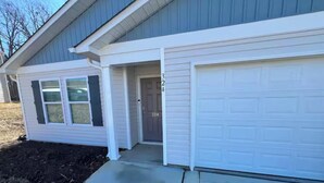 A single-story house with a garage, a front door, and a small porch. - Home featuring 3 Rooms 1 Bath Sleeps 6 Guest (Roxboro)