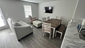 A modern living room with a sofa, a recliner, a dining table with chairs, a TV mounted on the wall, and a marble countertop. - Home featuring 3 Rooms 1 Bath Sleeps 6 Guest (Roxboro)