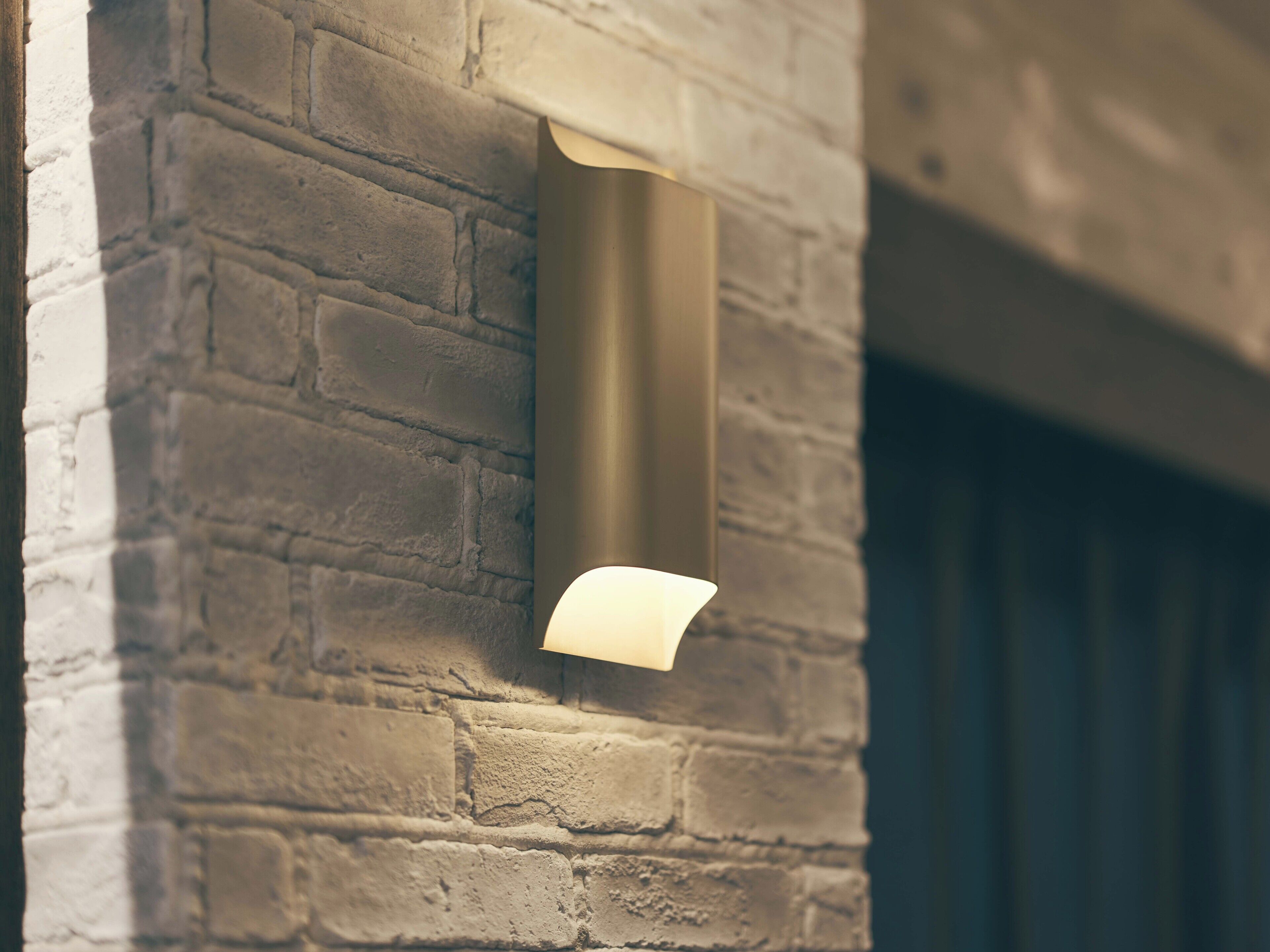 Un dettaglio di un muro di mattoni con una texture particolare, illuminato da un faretto metallico.