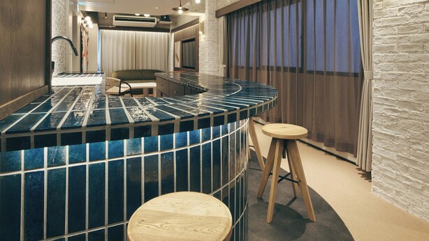 A modern bar area with a curved blue-tiled countertop, two wooden stools, and pendant lighting. - illi Lay Shibuya-Ebisu (Tokyo)