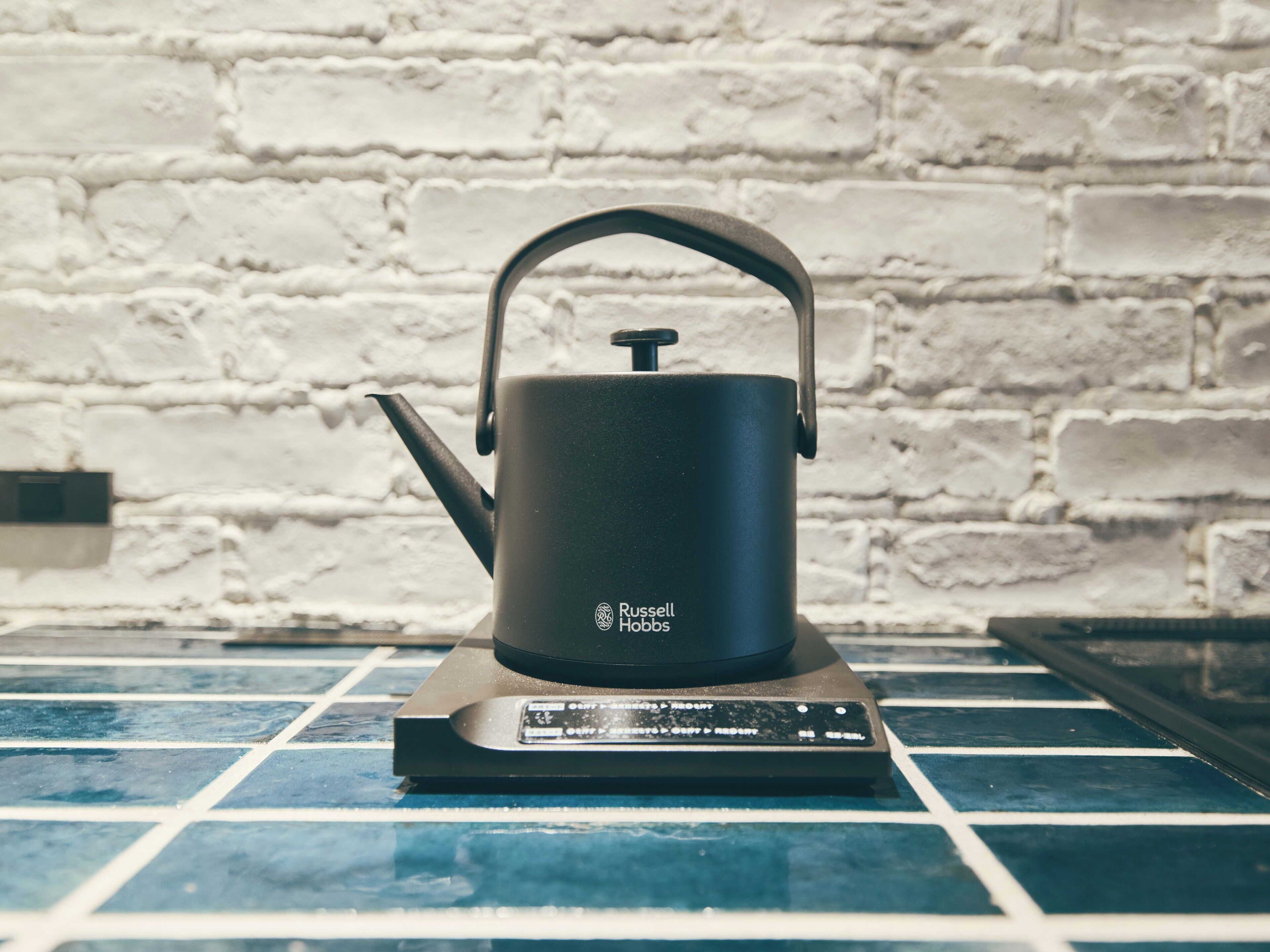 A Russell Hobbs electric kettle on a modern tiled countertop with a white brick wall in the background.