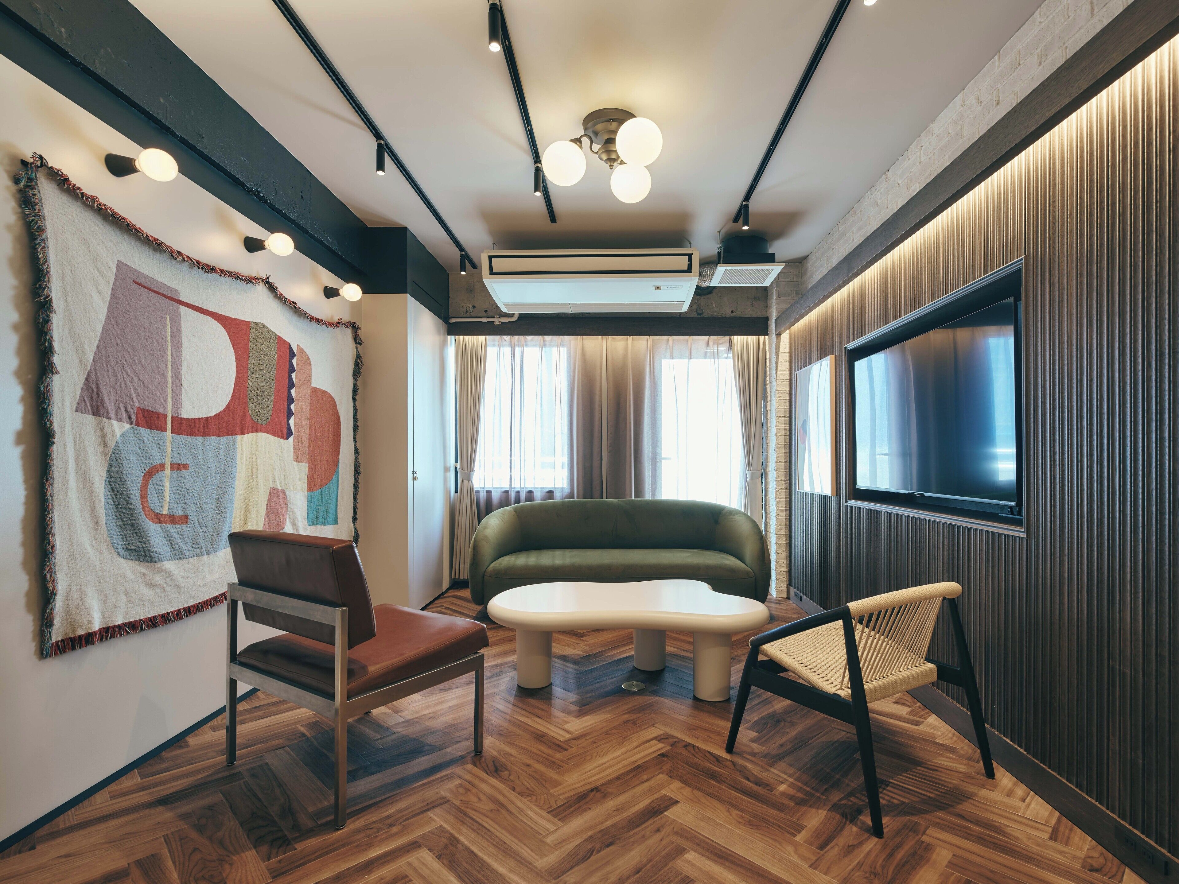 Una habitación moderna con un sofá verde, suelo de madera, televisor grande y techo con vigas y luces a la vista.