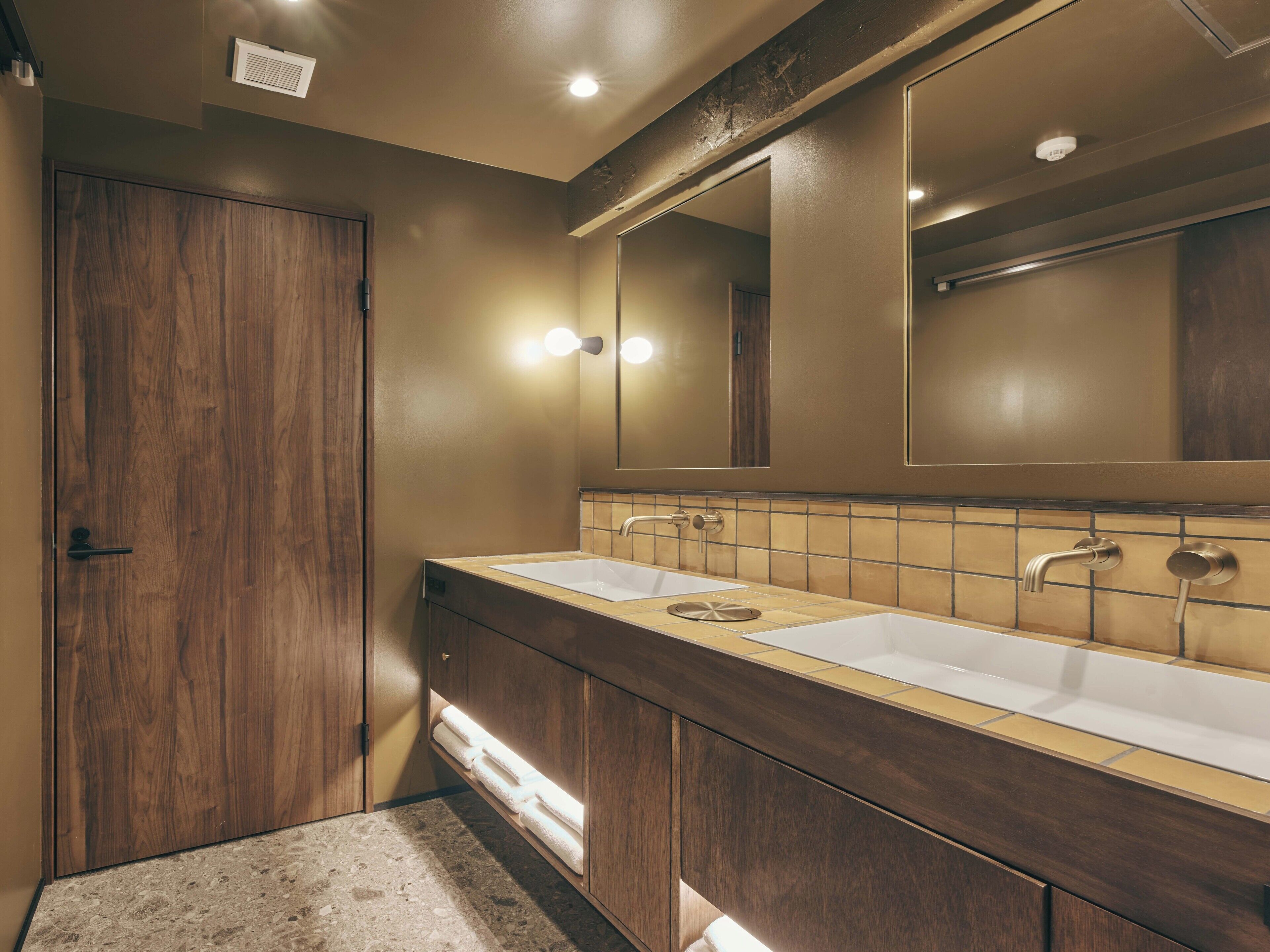 A bathroom with wooden cabinetry, two sinks, a large mirror, and a towel rack.