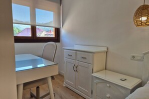 Een slaapkamer met een bed, nachtkastje, bureau, stoel, kledingkast en een raam met uitzicht.