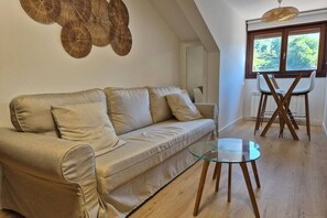 Een woonkamer met een bank, een glazen salontafel en een eethoek met stoelen.