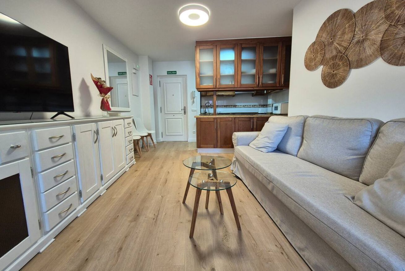A living room with a sofa, a TV, a glass coffee table, and wooden cabinets.