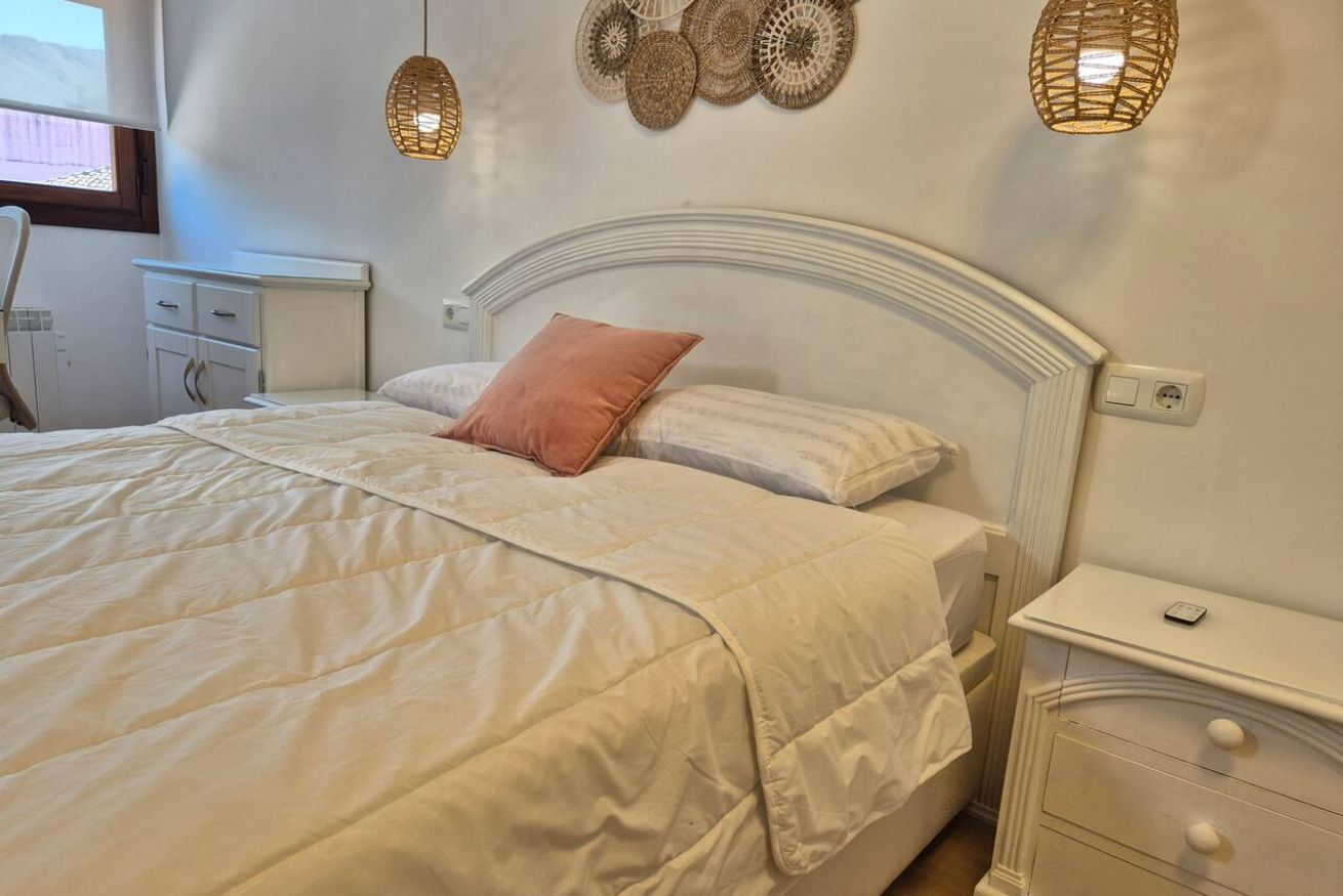 Ein ordentlich gemachtes Bett mit einem weißen Kopfteil, einem einzelnen rosafarbenen Kissen und einem weißen Nachttisch mit einer kleinen Uhr.