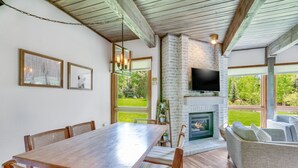 A dining area with a wooden table and chairs, a fireplace, and a television mounted on a brick wall.