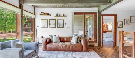 A spacious living room with a leather sofa, a grey armchair, and a patterned rug.