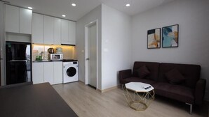 A modern apartment with a kitchen, a washing machine, a dark brown sofa, and abstract art on the wall. - Comfor apartment stay in HCM (Ho Chi Minh City)