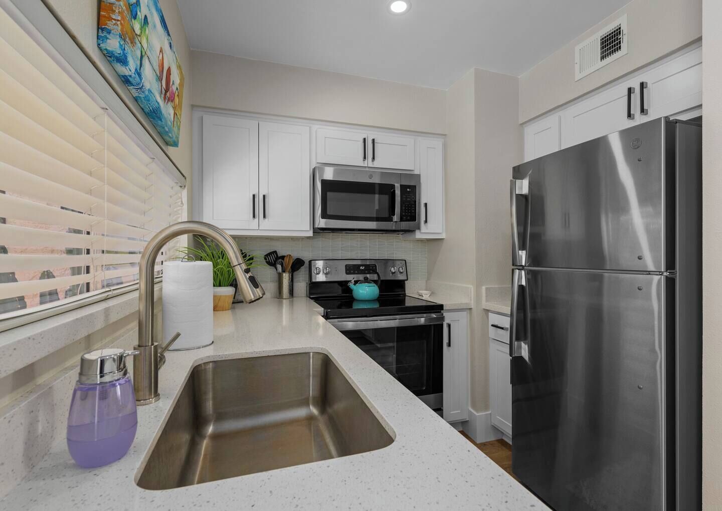A modern kitchen with stainless steel appliances, a large sink, and white cabinetry.