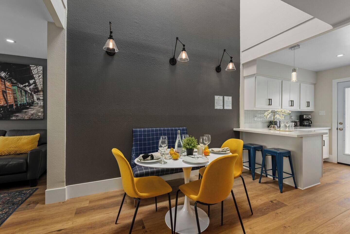A modern dining area with a dark accent wall, yellow chairs, and pendant lighting.