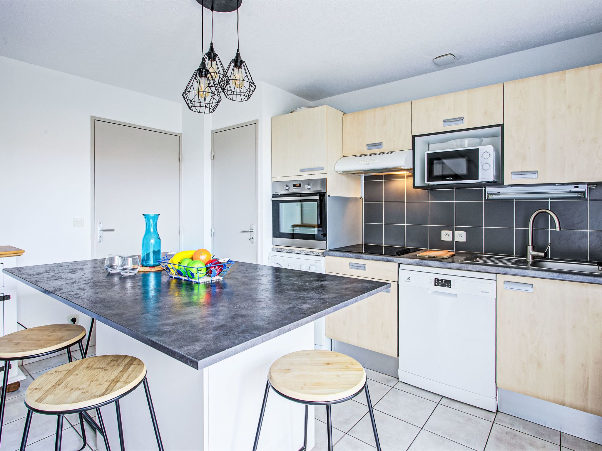 A modern kitchen with a central island, bar stools, a microwave, oven, and a sink.