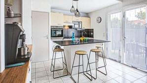Eine moderne Küche mit Kochinsel, Barhocker, einer Kaffeemaschine und einem großen Fenster.
