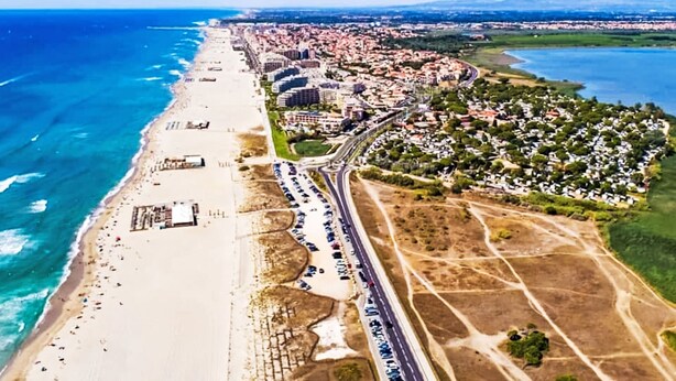 Luftaufnahme einer Küstenstadt mit Strand, Autobahn und Wohngebieten.