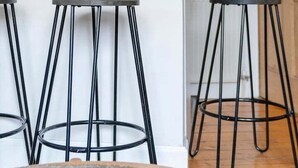 Une cuisine avec un plan de travail blanc, trois tabourets en métal noir, une horloge murale et trois tableaux encadrés.