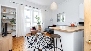 Un salon moderne avec un plancher en bois, un tapis à motifs, un canapé, une table basse et un téléviseur posé sur un meuble en bois.