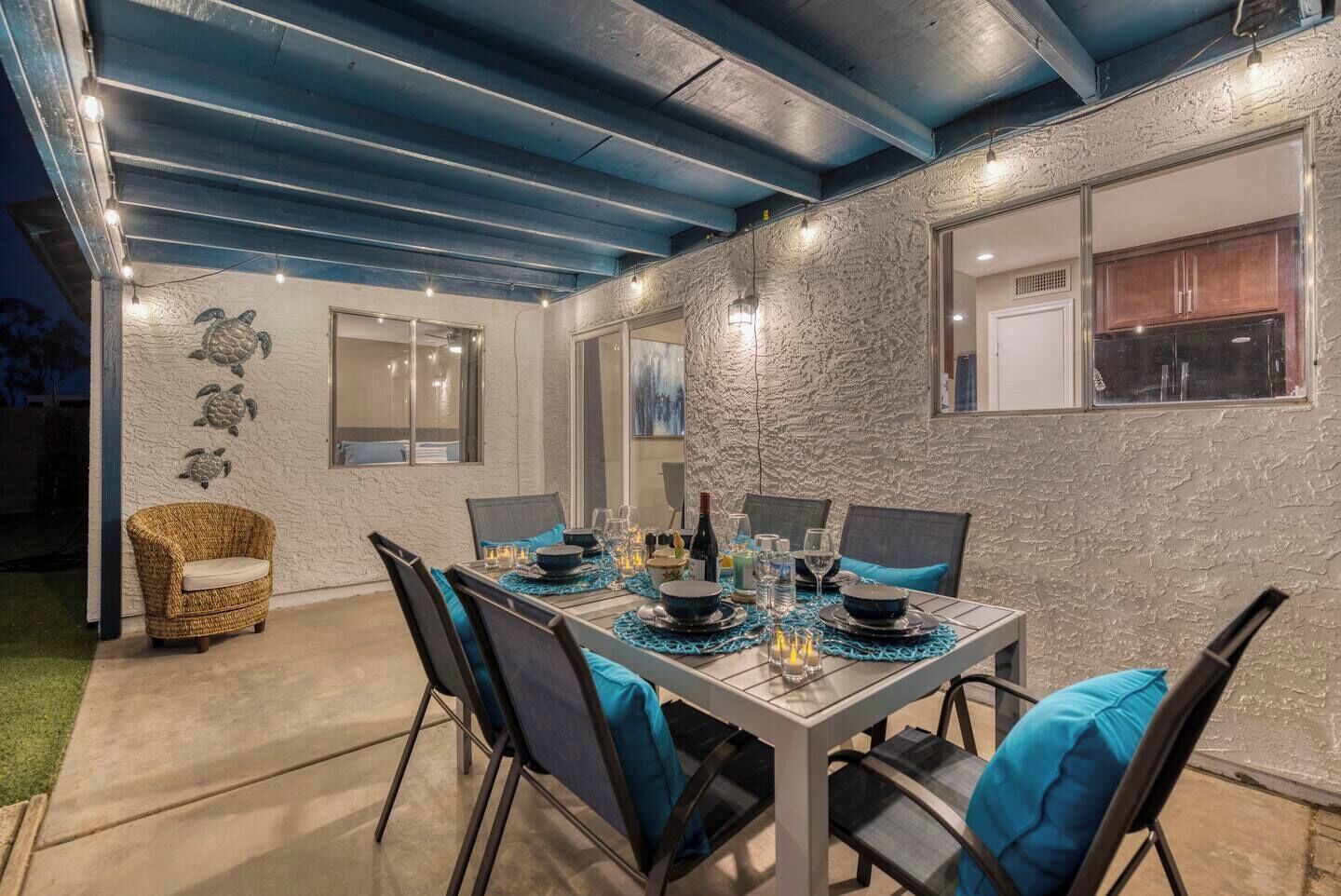 An outdoor dining area with a table set for six, surrounded by chairs with blue cushions.