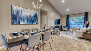 A modern living room with a dining area, featuring a large abstract painting, a chandelier, and a view of the outdoors. - Blue Oasis with Private Heated Pool at NO COST (Tempe)