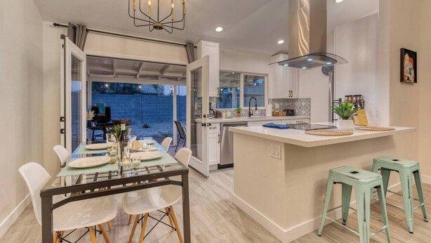 A modern kitchen with an island, a dining area with a glass table, and a view of the backyard.