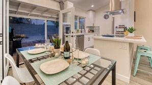 A modern kitchen with white cabinets, a built-in oven, and a dining area with a glass table and chairs.