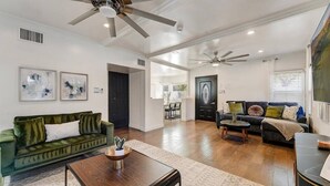 A spacious living room with a green sofa, a wooden coffee table, and a dark armchair. There are ceiling fans and a large window with blinds. - Fabulous entertainers Paradise! Pool & Spa (Phoenix)