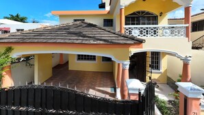 A two-story house with a tiled roof, a balcony with white railings, and a gated entrance. - Spacious and secure villa 5 minutes from the beach (Puerto Plata)