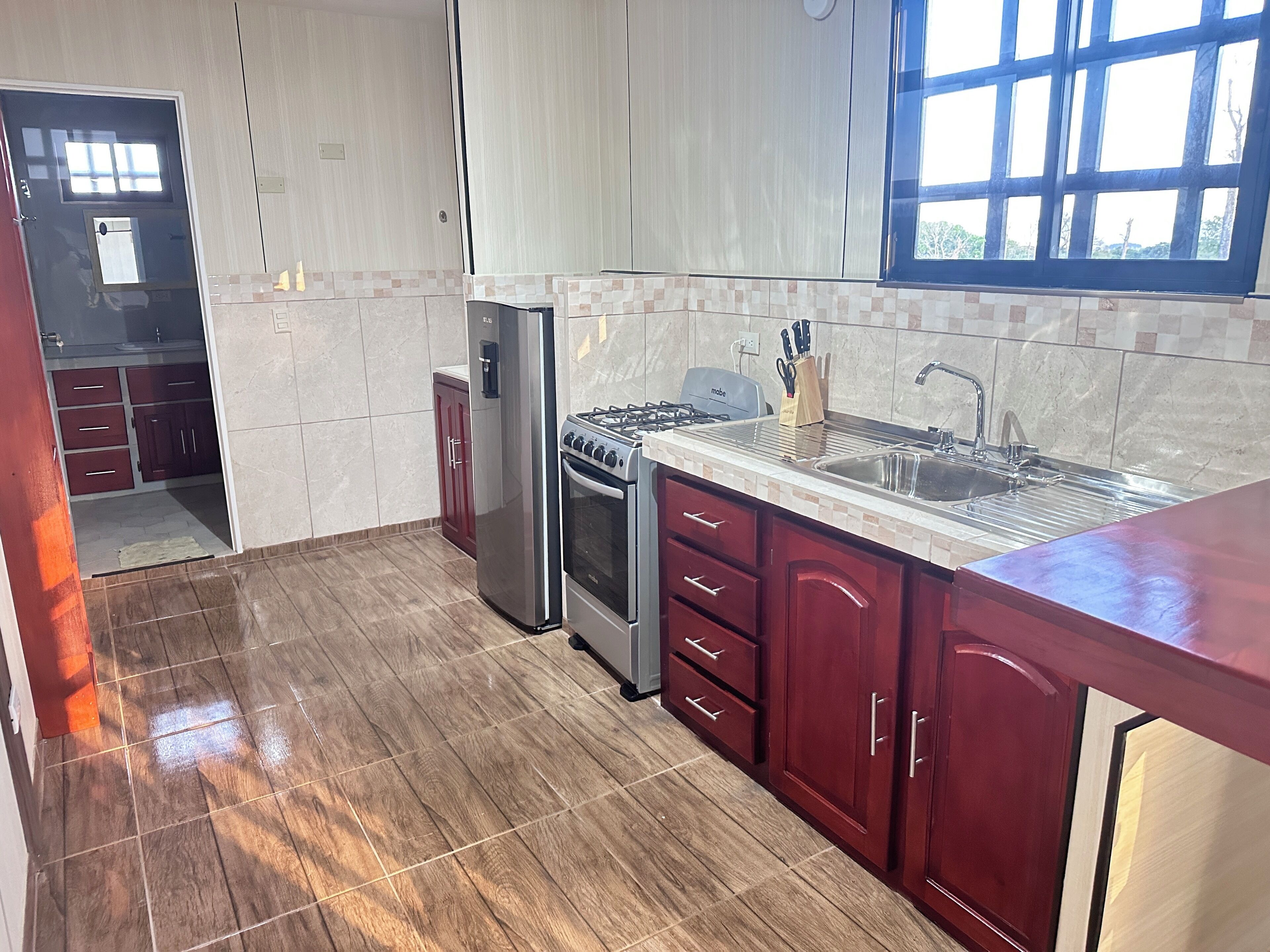 A kitchen with a stainless steel refrigerator, a gas stove, and a sink. There is a window providing natural light.