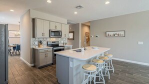 A modern kitchen with a central island, bar stools, and a dining area with a table and chairs.