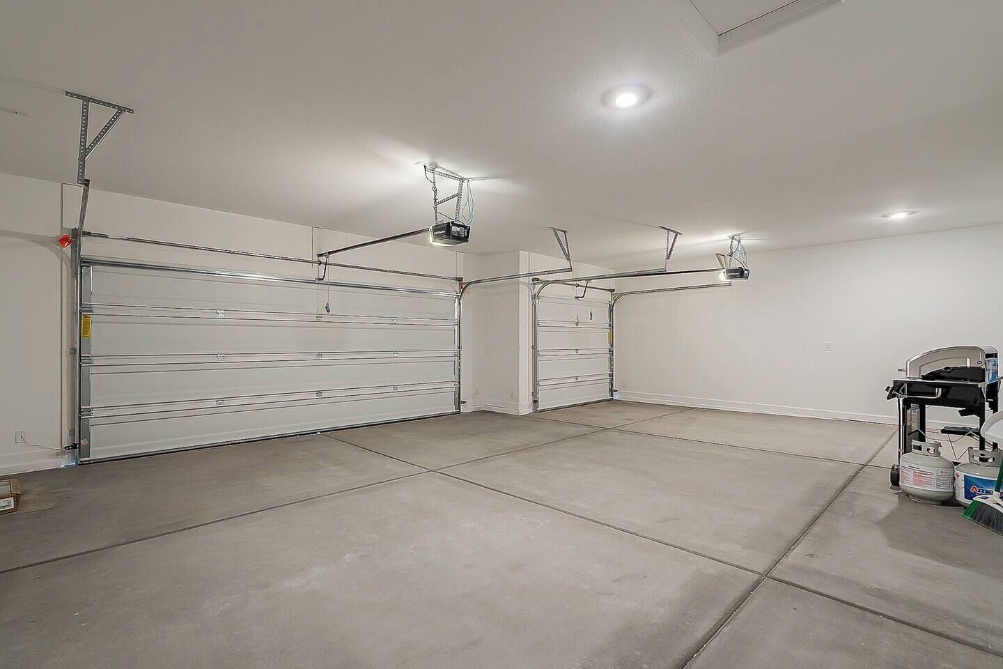 Eine saubere, leere Garage mit drei großen Garagentoren, Deckenbeleuchtung und einem Werkswagen mit Gasbehältern.