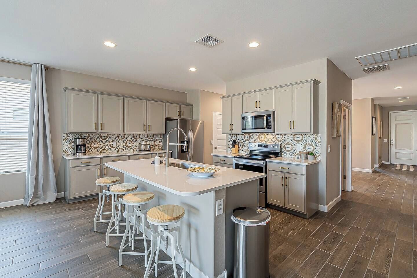 Et moderne køkken med en central ø, barstole, rustfrie hvidevarer og et mønstret backsplash.