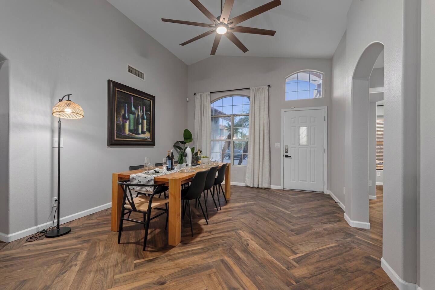 A dining area with a wooden table set for six, a floor lamp, and a ceiling fan.