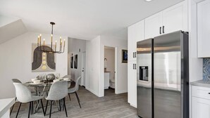 A modern kitchen with a large stainless steel refrigerator, white cabinetry, and a dining area with grey chairs and a chandelier. - The BEST Executive home in Palm Desert!4 Bedrooms (Palm Desert)