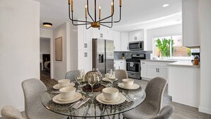 A modern kitchen with white cabinets, stainless steel appliances, and a dining area with a glass table set for four. - The BEST Executive home in Palm Desert!4 Bedrooms (Palm Desert)
