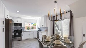 A modern kitchen with white cabinets, stainless steel appliances, and a dining area with a glass table and chairs. - The BEST Executive home in Palm Desert!4 Bedrooms (Palm Desert)