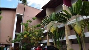 A multi-story building with a beige exterior, surrounded by lush greenery and parked cars. - Charming apartment on Cumbuco Beach, Ceara, Brazil (Praia de Cumbuco Caucaia)