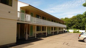 Um motel com área de estacionamento coberta e uma fileira de quartos com portas e janelas verdes.