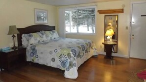 Un dormitorio con cama, mesita de noche, lámpara, ventana y puerta.