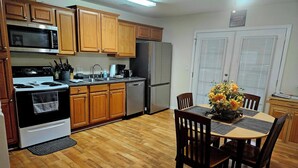 A kitchen with wooden cabinets, a microwave, stove, refrigerator, and a dining table with chairs.