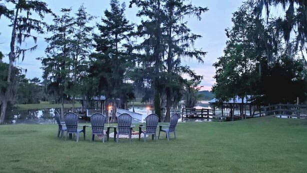 A grassy area with a table and chairs, surrounded by trees and a wooden fence.