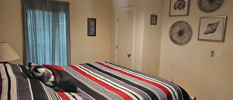 A bedroom with a bed, a ceiling fan, a window with curtains, and wall decorations including framed pictures and a sign.