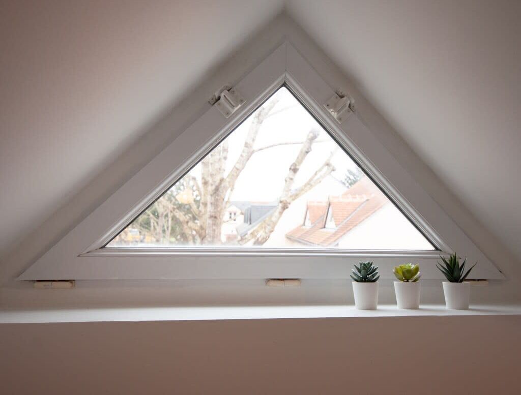 Un tragaluz triangular con tres plantas en macetas sobre un alféizar.