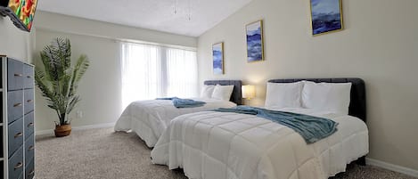 Une chambre d’hôtel avec deux lits, un ventilateur de plafond, une télévision, une plante en pot et des œuvres d’art accrochées aux murs.