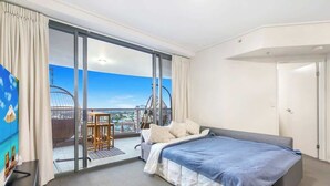 A hotel room with a bed, a small table, and a view of a cityscape through a large window. - Arcade In The Sky- Views, Games & Vibes (Brisbane City)