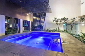 Una piscina interna moderna con un elemento d'acqua illuminato di blu, circondata da un giardino curato e un'architettura contemporanea.