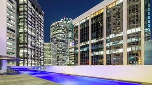 A modern hotel with a pool area, surrounded by high-rise buildings and illuminated at night. - Arcade In The Sky- Views, Games & Vibes (Brisbane City)