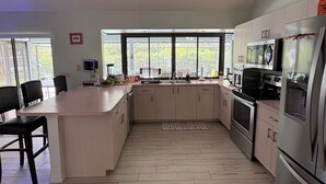 Une cuisine moderne dotée d’un grand îlot central, d’appareils électroménagers en acier inoxydable et offrant une vue dégagée par les fenêtres.