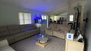 Un salon spacieux avec une table basse en verre, deux canapés, un ventilateur de plafond et un grand aquarium.