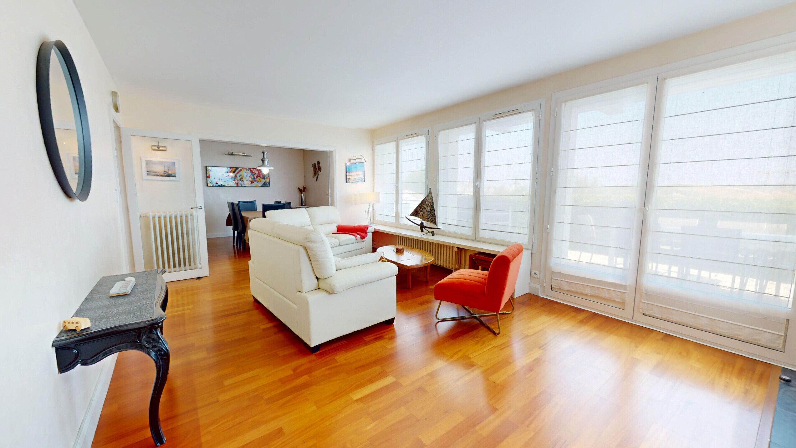 A spacious living room with a white sofa, a red chair, and a dining area with a table and chairs.