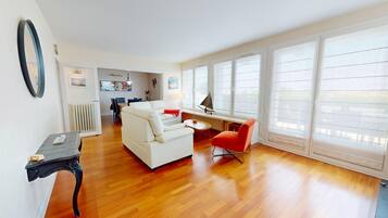 A spacious living room with a white sofa, a red chair, and a dining area with a table and chairs.